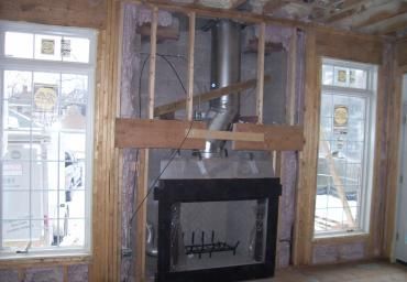 Interior wall under construction with a fireplace insert between two windows