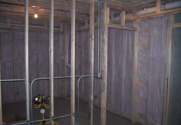 Unfinished basement with exposed framing, insulation, and a small work light on the floor.