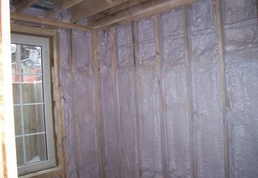 Insulated wall with exposed framing beside a small window in a renovated interior