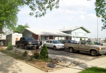 Suburban house with three parked pickup trucks in the driveway under leafy trees