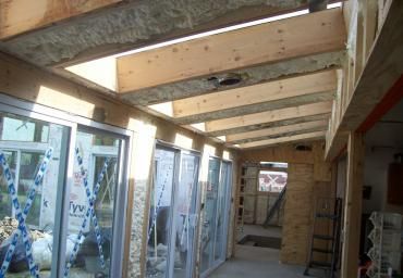 Wood-framed corridor with glass storefronts and exposed ceiling beams under construction