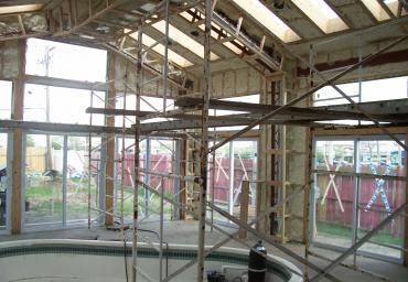 Scaffolding inside a bright, unfinished building with large windows and exposed beams