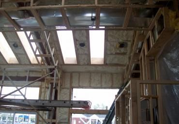 Interior of a building under construction with exposed ceiling beams, insulation, and scaffolding