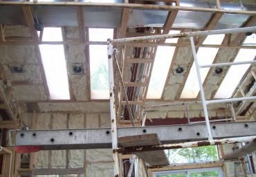 Damaged building interior with exposed wooden roof beams and broken ceiling panels