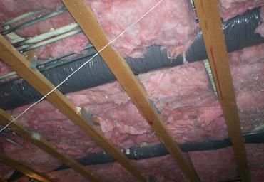 Exposed attic framing with pink fiberglass insulation between wooden rafters.