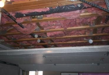 Exposed ceiling framing with pink insulation and a metal duct running across the top of a room