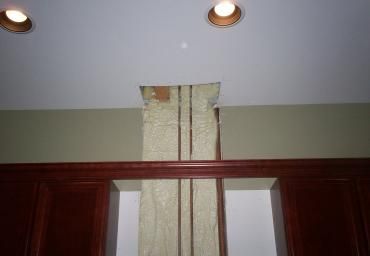 Curtained window centered above dark wood trim, with two ceiling recessed lights on a pale wall.