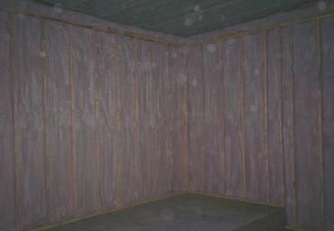 Dim wooden corner with vertical planks and a low bench or platform.