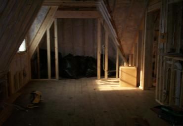 Unfinished attic with exposed wooden framing and a dark pile of materials near the back wall.