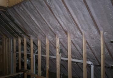 Attic with exposed wooden rafters and silver insulation under a pitched roof