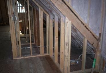 Attic interior with exposed wood framing, slanted roof beams, and a partially framed wall opening