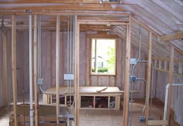 Interior of an unfinished room with exposed wooden framing, insulation, and electrical wiring under construction