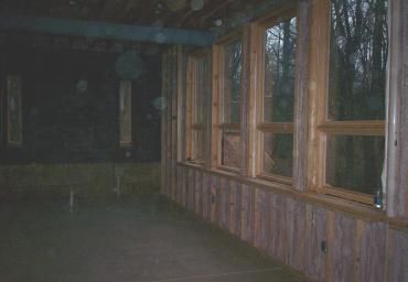 Dim wooden room with large windows overlooking trees at dusk