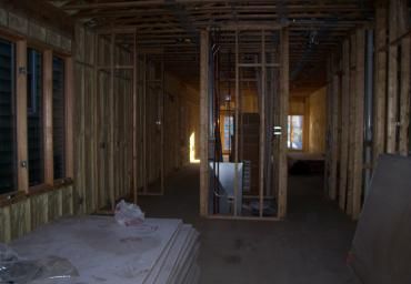 Unfinished house interior with exposed wooden framing, drywall stacks, and light from windows.