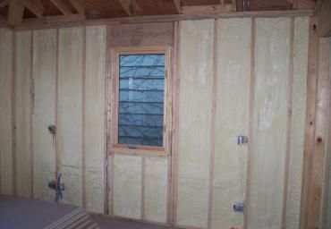 Unfinished insulated interior wall with a small window and exposed framing planks