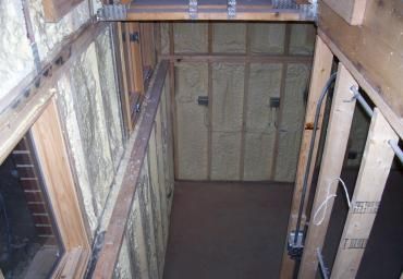 Interior view of an unfinished elevator shaft with exposed framing and a closed door at the far end