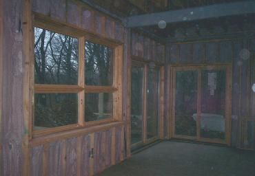 Dim wooden porch or sunroom with large windows and glass doors, viewed at dusk.