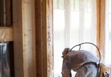 Worker bent over in an unfinished room near a bright window and wooden framing