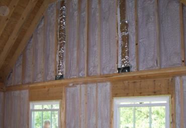 Interior of an unfinished A-frame wall with exposed insulation and two small windows.