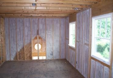 Small unfinished wooden room with bare floor, exposed beams, and two windows letting in daylight.