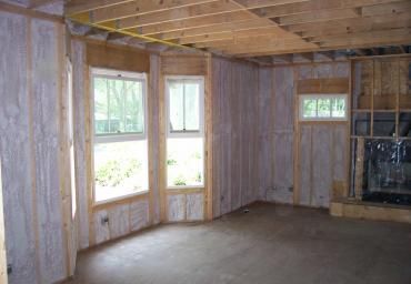 Empty wood-paneled room with windows, concrete floor, and a fireplace