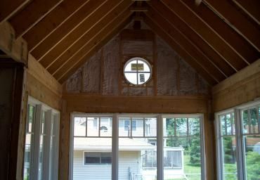 Wooden gazebo interior with a peaked ceiling and round window overlooking houses outside