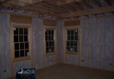 Empty unfinished room with wood-paneled walls, exposed beams, and three windows at night