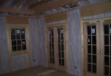 Unfinished room with exposed insulation, wood framing, and several tall windows or doors along the wall