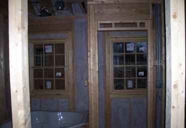 Wooden-framed interior under construction, with a tub and multiple windows or doors visible.