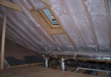 Insulated attic with exposed rafters, ductwork, and a small roof window.