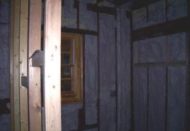 Dim wooden interior with a small window and a doorway, lit by a faint flash.