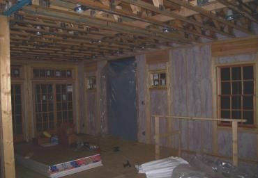 Dim unfinished room with exposed ceiling beams, windows, and construction materials on the floor.