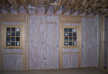 Wooden interior wall with two small windows and a central door under exposed ceiling beams