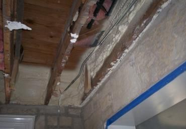 Damaged ceiling with exposed wooden beams and cracked plaster above a doorway