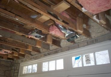 Exposed wooden ceiling joists with pink insulation above a row of white windows in a room under renovation