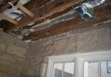 Partially demolished room with exposed ceiling beams and insulation above a window