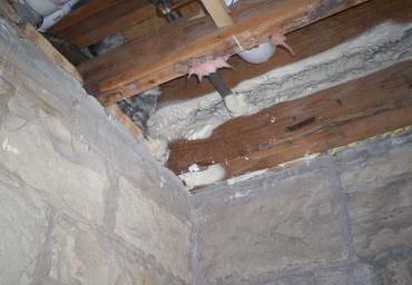 Damaged ceiling with exposed wooden beams, cracked plaster, and debris in an old stone room
