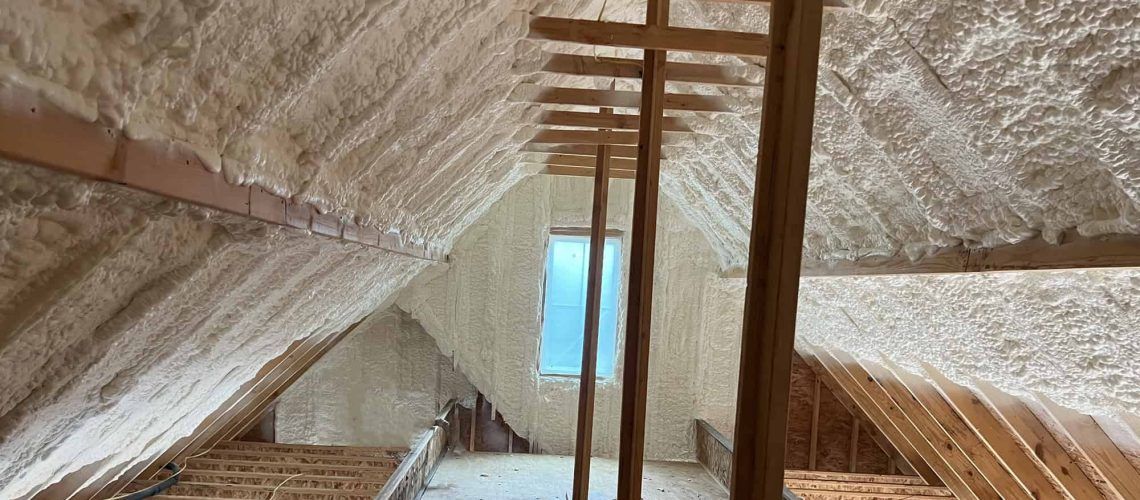 Insulated attic interior with exposed rafters, wooden beams, and a small window at the far end