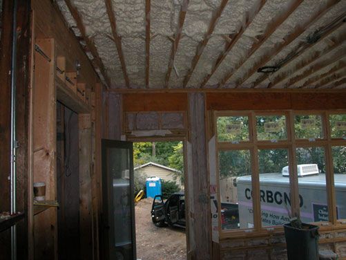 Interior of a partly finished room with exposed framing, windows, and a view of construction materials outside