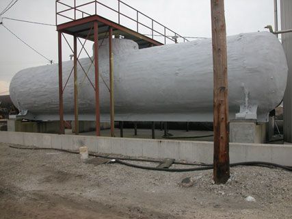 Large gray industrial storage tank on a concrete base in a fenced outdoor yard