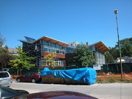 Modern building with glass balconies behind parked cars and a blue tarp covering an object by the street