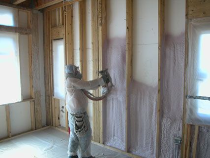 Person spraying foam insulation on interior walls of a house under construction