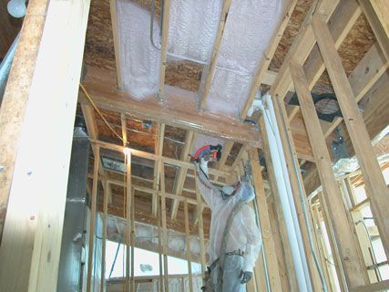 Construction worker installing insulation in a wooden house frame, viewed from inside an unfinished room