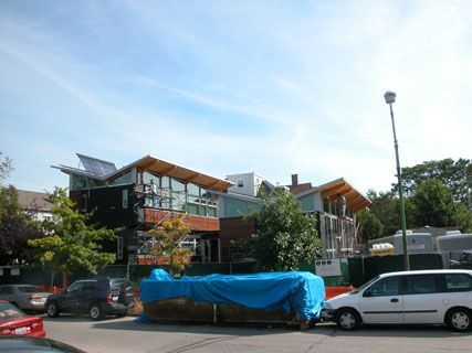 Street view of modern houses with parked cars and a blue tarp-covered vehicle under a clear sky
