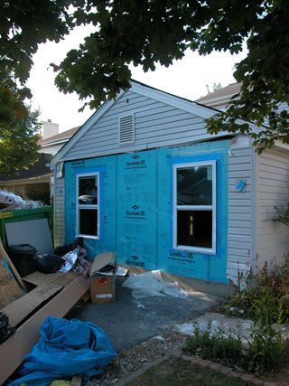 Blue house under construction with two windows, front door, and scattered building materials in the yard