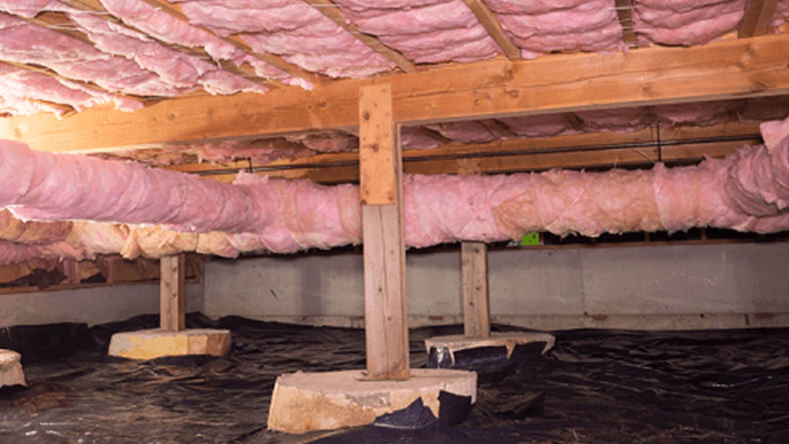 Pink insulation and wooden beams in an unfinished attic crawlspace under a house