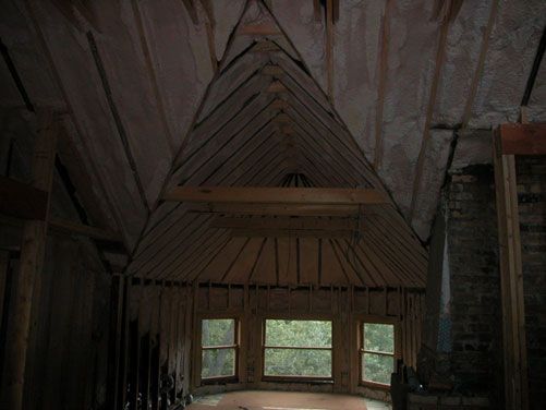 A rustic wooden cabin interior with a steep A-frame roof and small windows showing trees outside