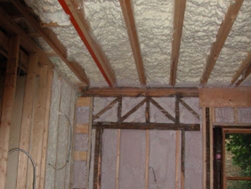 Interior wall under construction with spray foam insulation and exposed wooden beams