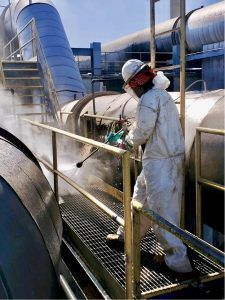 A man in a protective suit is cleaning a pipe in a factory.