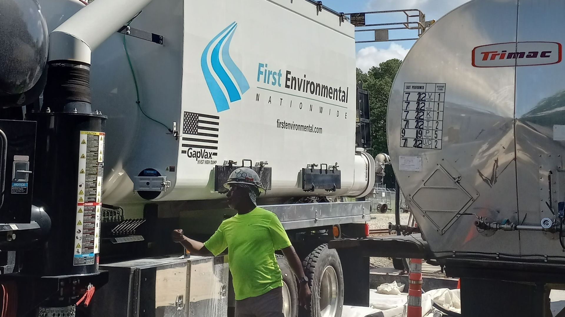 A man in a green shirt is standing in front of a first environmental truck.